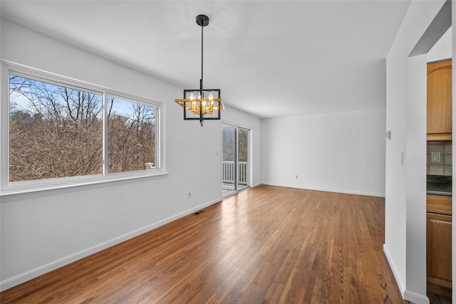 unfurnished dining area with a chandelier, visible vents, baseboards, and wood finished floors