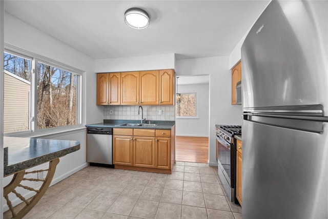 kitchen with a sink, dark countertops, backsplash, appliances with stainless steel finishes, and light tile patterned flooring