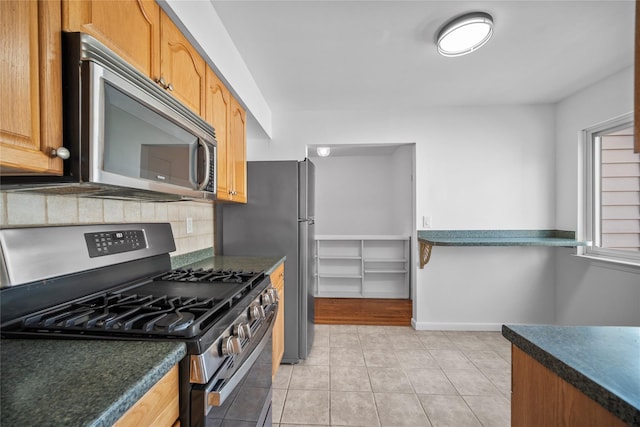 kitchen with decorative backsplash, dark countertops, appliances with stainless steel finishes, and light tile patterned flooring