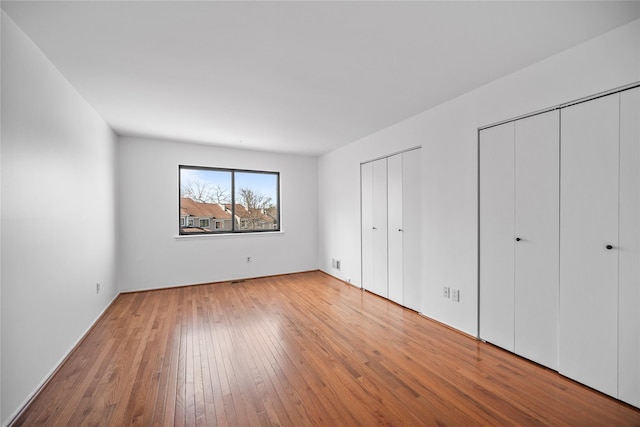 unfurnished bedroom with two closets and hardwood / wood-style flooring