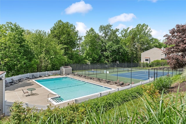 community pool with a patio area, a tennis court, and fence