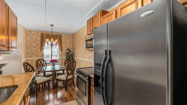 kitchen with wainscoting, appliances with stainless steel finishes, wallpapered walls, and a textured ceiling