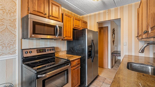 kitchen featuring light tile patterned floors, wallpapered walls, a sink, stainless steel appliances, and a textured ceiling