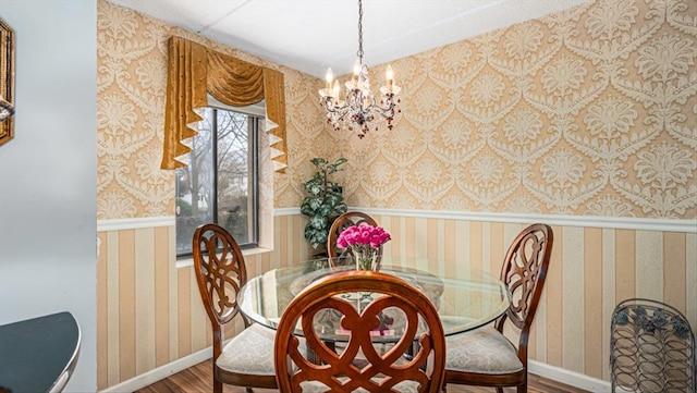 dining space with a notable chandelier, wood finished floors, wainscoting, wallpapered walls, and baseboards