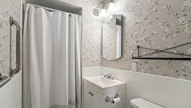 full bath featuring toilet, curtained shower, tile walls, wainscoting, and wallpapered walls