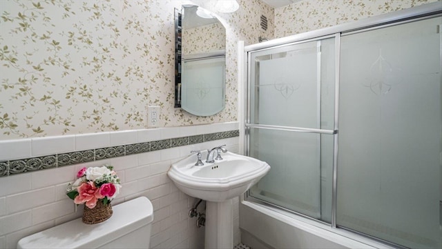 full bathroom featuring visible vents, a wainscoted wall, toilet, tile walls, and wallpapered walls