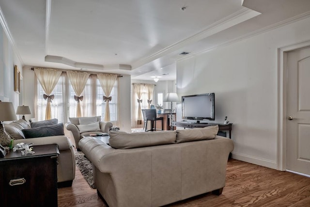 living room with visible vents, crown molding, baseboards, a tray ceiling, and wood finished floors