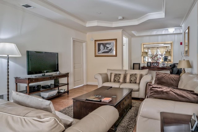 living room featuring visible vents, crown molding, baseboards, a tray ceiling, and wood finished floors