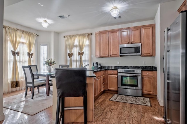 kitchen with a peninsula, visible vents, dark wood-type flooring, and appliances with stainless steel finishes