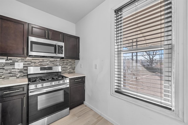 kitchen featuring tasteful backsplash, stainless steel appliances, dark brown cabinetry, light countertops, and baseboards