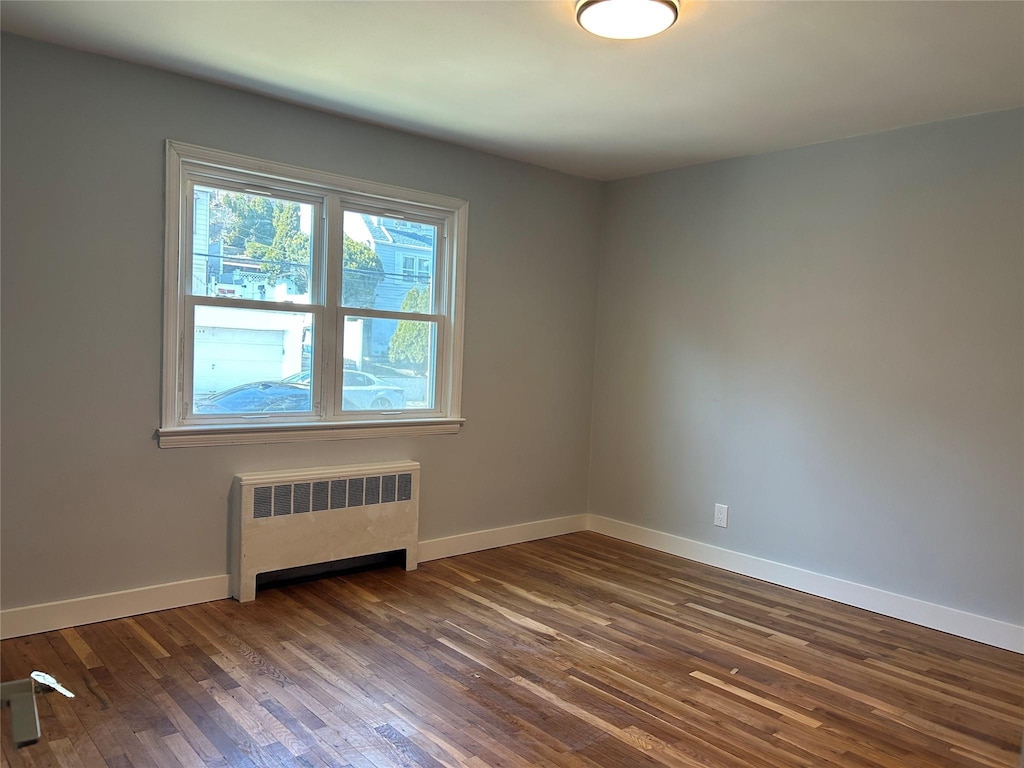 unfurnished room featuring baseboards, dark wood-type flooring, and radiator heating unit