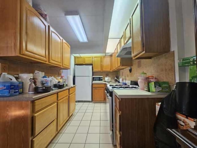 kitchen featuring backsplash, under cabinet range hood, light countertops, light tile patterned floors, and appliances with stainless steel finishes