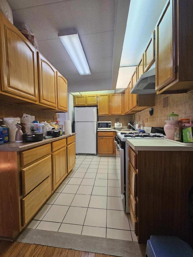 kitchen featuring under cabinet range hood, decorative backsplash, gas range, and freestanding refrigerator