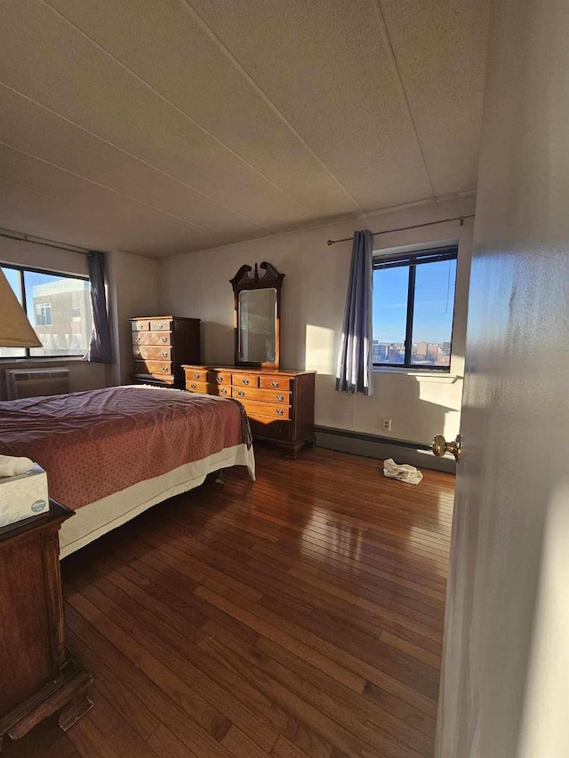 bedroom featuring multiple windows, a wall mounted AC, a baseboard heating unit, and hardwood / wood-style floors