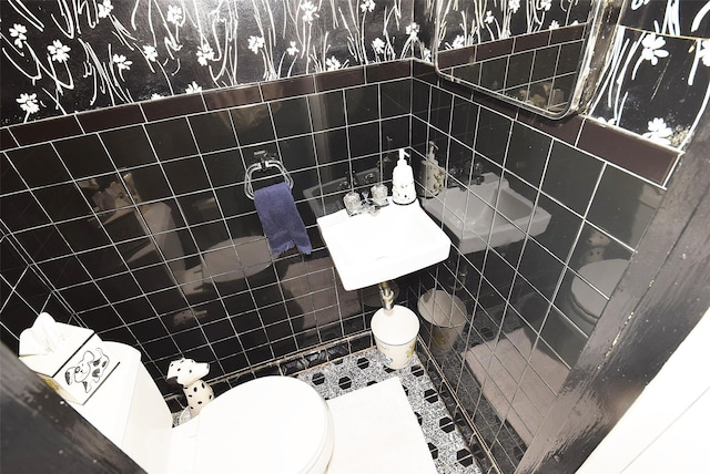 bathroom featuring a sink, toilet, tile walls, and wallpapered walls