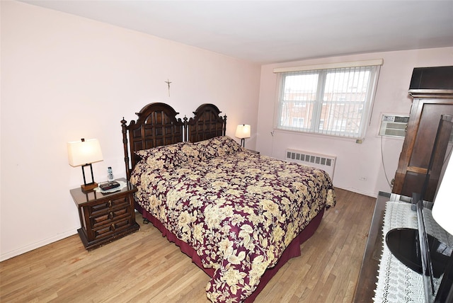 bedroom featuring radiator heating unit, baseboards, light wood-type flooring, and a wall mounted air conditioner