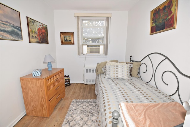 bedroom with radiator heating unit, cooling unit, baseboards, and light wood finished floors