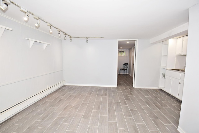 empty room featuring wood finish floors, baseboards, baseboard heating, and track lighting