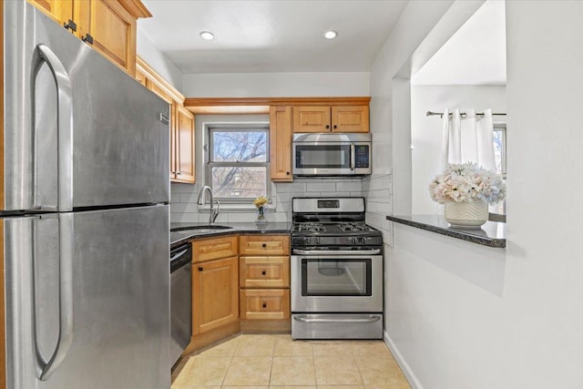 kitchen featuring backsplash, dark stone countertops, appliances with stainless steel finishes, light tile patterned flooring, and a sink