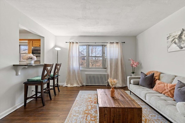 living room featuring baseboards, a textured ceiling, dark wood-style floors, and radiator heating unit