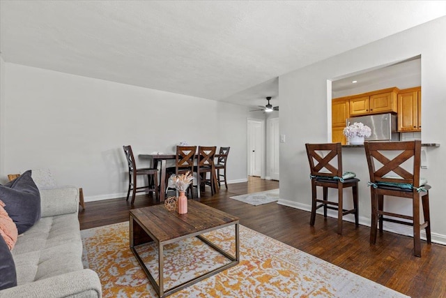 living room with baseboards, dark wood-type flooring, and ceiling fan