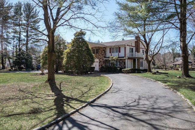 view of front of property with a front lawn, a balcony, driveway, and a chimney