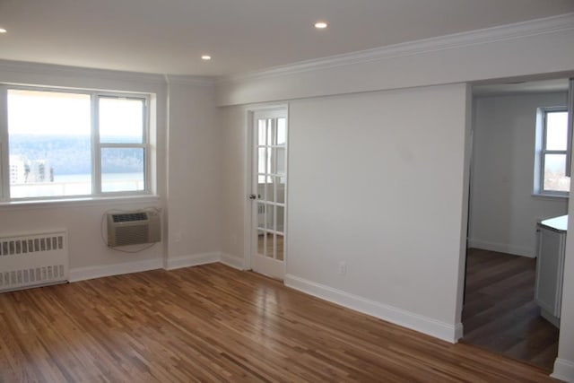 empty room featuring ornamental molding, wood finished floors, radiator heating unit, a wall unit AC, and baseboards