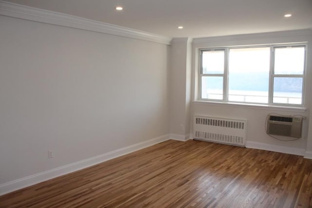 spare room with crown molding, baseboards, radiator heating unit, a wall unit AC, and wood finished floors