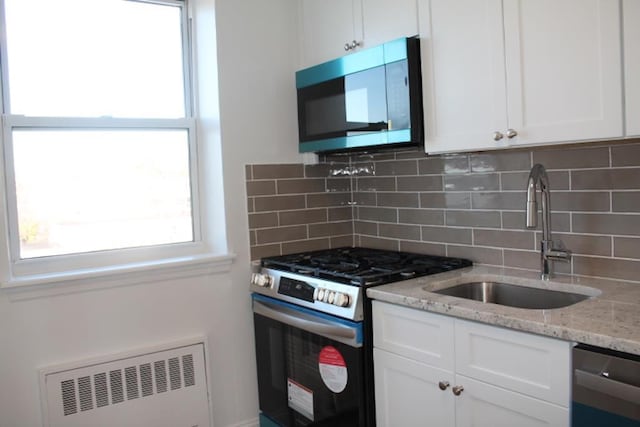 kitchen featuring radiator, light stone countertops, appliances with stainless steel finishes, white cabinets, and a sink