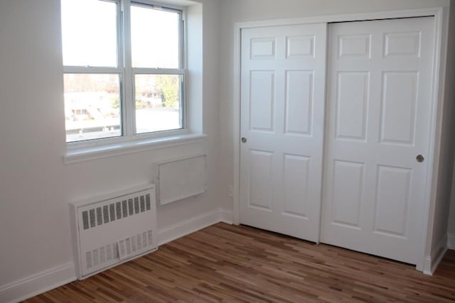 unfurnished bedroom with a closet, radiator, baseboards, and wood finished floors