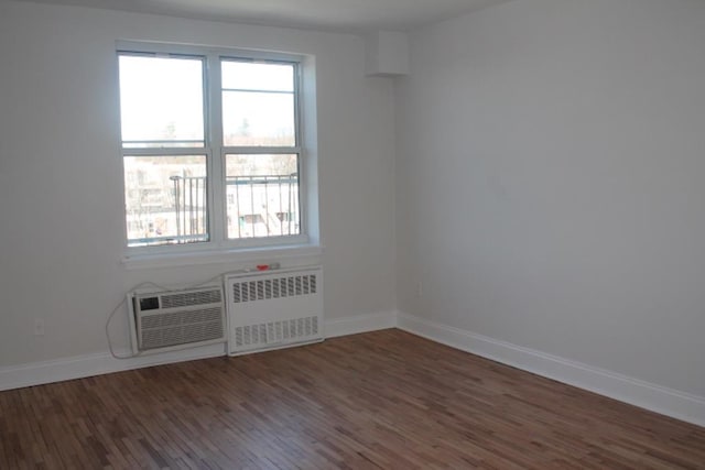 unfurnished room with radiator heating unit, wood finished floors, baseboards, and a wall mounted AC