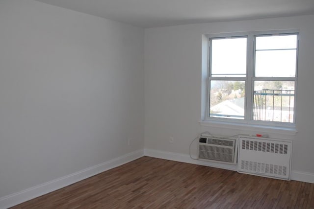 unfurnished room with radiator, an AC wall unit, baseboards, and wood finished floors