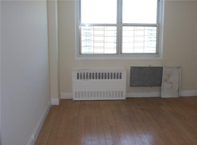 spare room with a healthy amount of sunlight, radiator heating unit, and hardwood / wood-style flooring