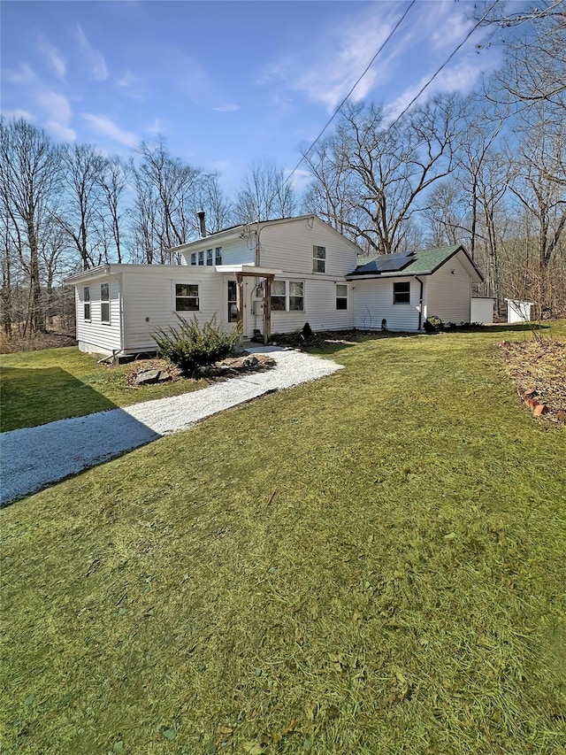 rear view of property featuring gravel driveway, a yard, and roof mounted solar panels