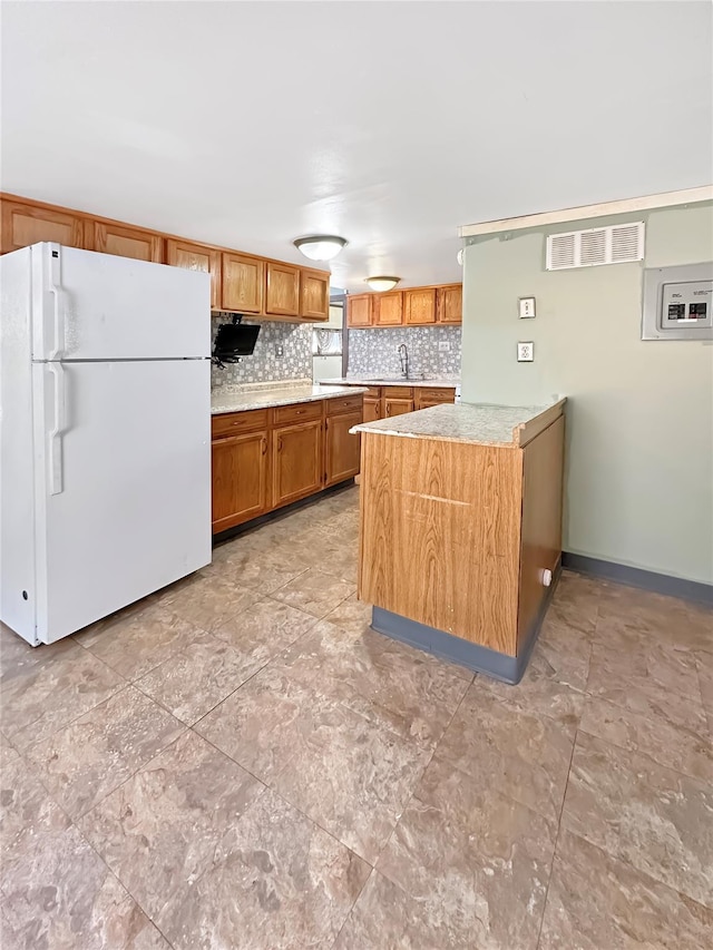 kitchen featuring visible vents, brown cabinets, a sink, tasteful backsplash, and freestanding refrigerator