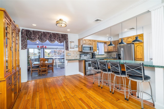 kitchen featuring light wood-type flooring, visible vents, a breakfast bar, appliances with stainless steel finishes, and decorative backsplash