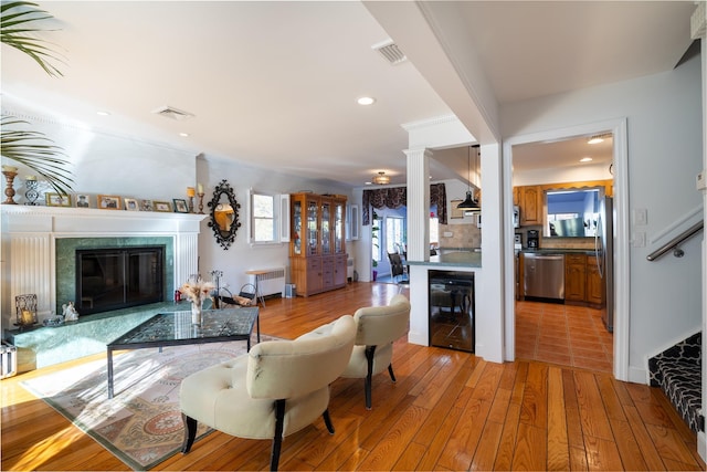 living area with radiator, visible vents, a fireplace, wine cooler, and light wood-type flooring