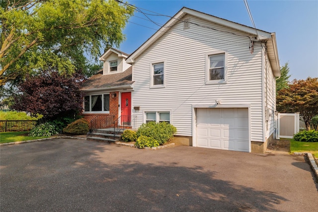 tri-level home featuring a garage, aphalt driveway, and fence