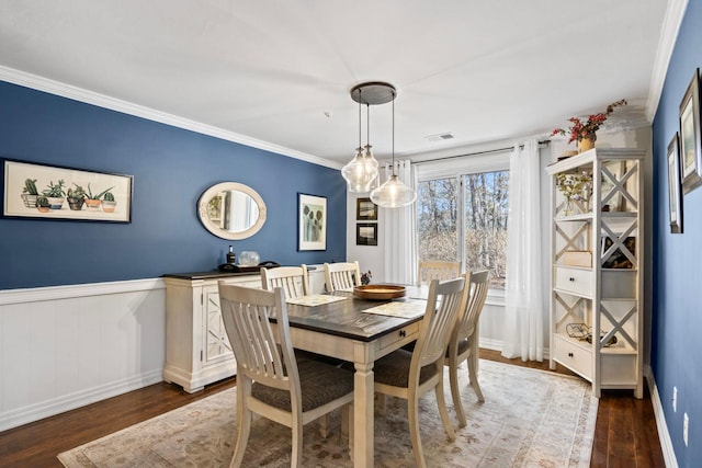 dining room with a wainscoted wall, dark wood-type flooring, visible vents, and ornamental molding