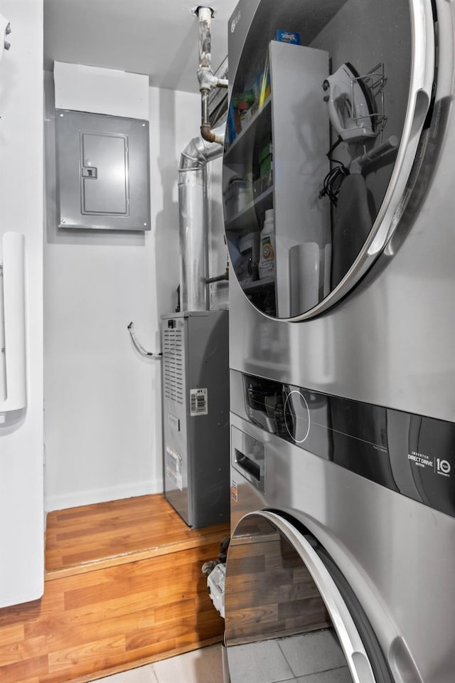 laundry room with baseboards, stacked washer and dryer, electric panel, laundry area, and wood finished floors