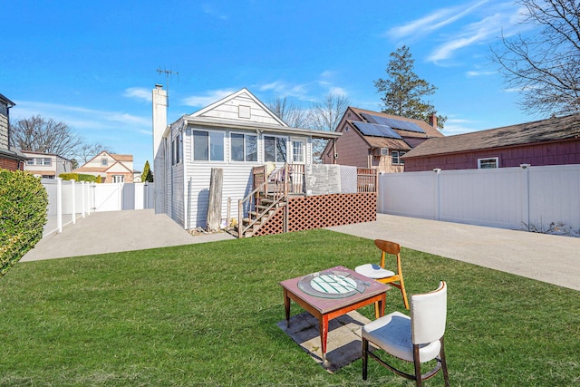 back of house with a chimney, a deck, a yard, a patio area, and a fenced backyard