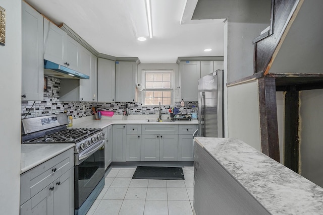 kitchen featuring gray cabinetry, under cabinet range hood, light countertops, appliances with stainless steel finishes, and a sink