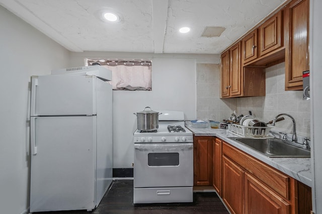 kitchen featuring white appliances, brown cabinetry, a sink, light countertops, and backsplash