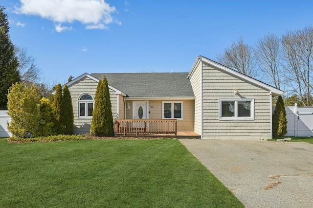 view of front of home with fence, a front yard, roof with shingles, a deck, and driveway