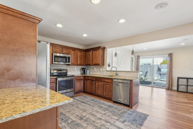 kitchen with tasteful backsplash, light wood-style floors, appliances with stainless steel finishes, a peninsula, and brown cabinetry