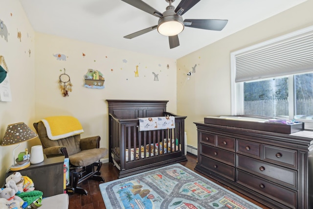 bedroom featuring a baseboard heating unit, a crib, wood finished floors, and a ceiling fan