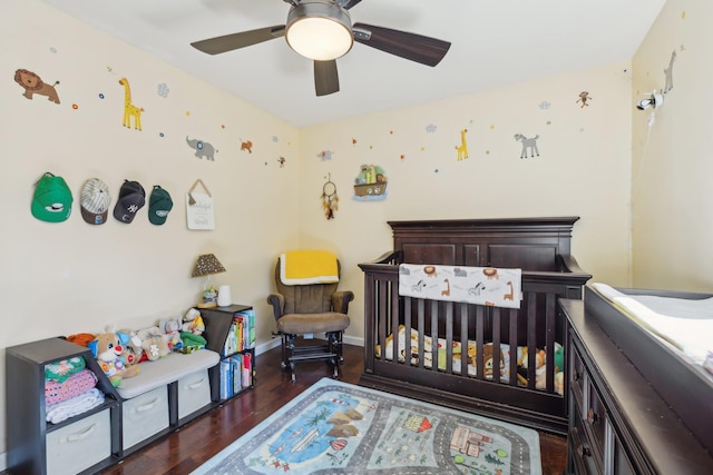 bedroom with a crib, wood finished floors, baseboards, and ceiling fan