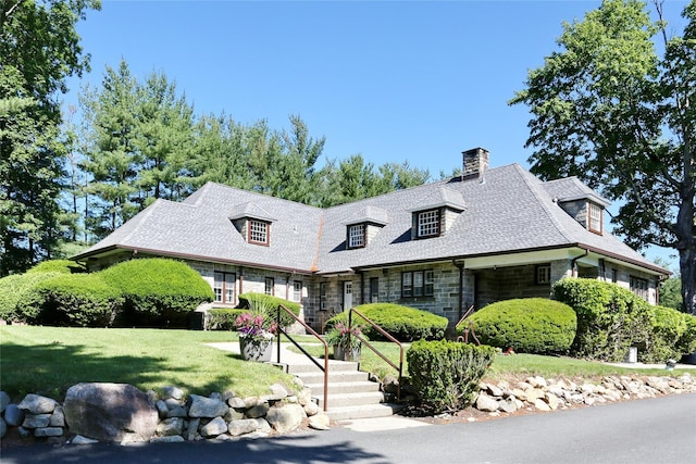 view of front of house featuring stone siding, a chimney, and a front lawn