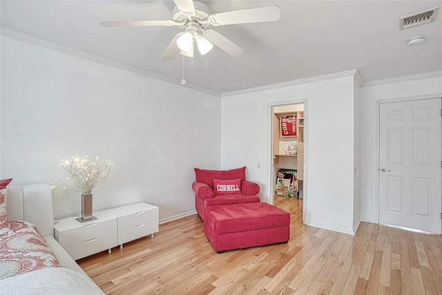 sitting room with visible vents, light wood-style floors, ornamental molding, and a ceiling fan