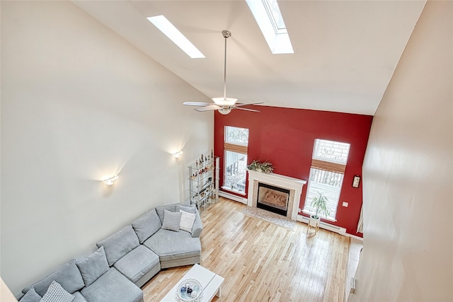 living area with high vaulted ceiling, wood finished floors, a skylight, a fireplace, and baseboard heating